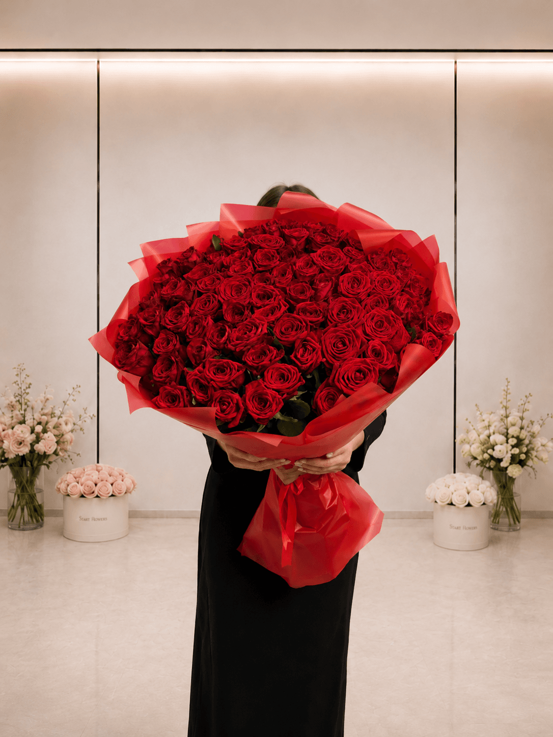 Букет из 101 красной розы в алой упаковке на фоне офиса Start Flowers